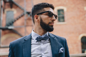 Man wearing black walnut polarised sunglasses in front of blurry brick wall